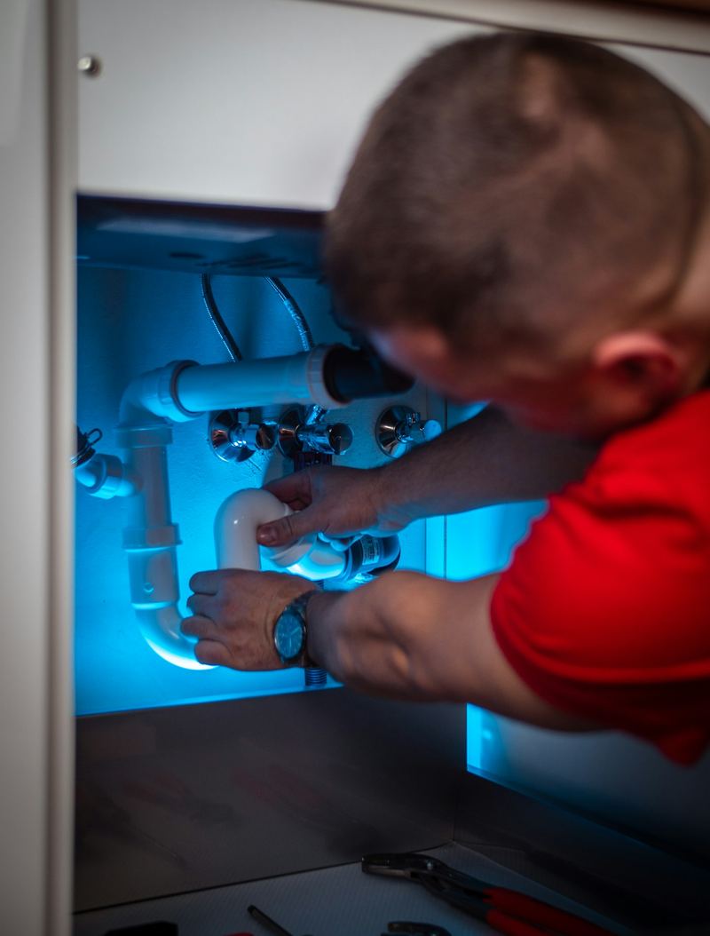 Mavi ışıklı lavabo altında gider tesisatını inceleyen tesisatçı